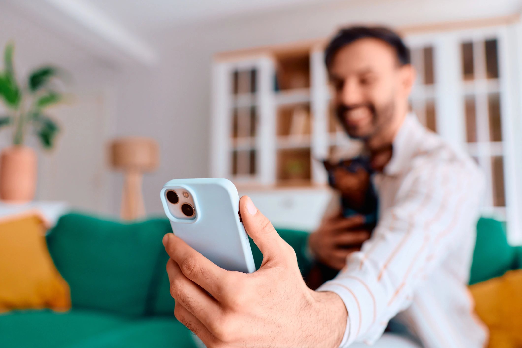 Man holding a small dog while using a smartphone at home